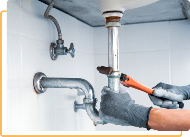 A plumbing services expert in Roseville adjusts a silver pipe under a sink.