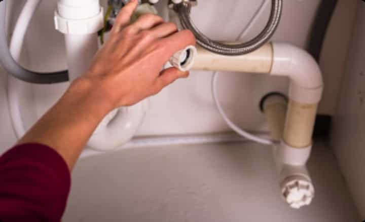A residential plumbing expert's hand inspects a valve on a PVC pipe attached to a silver hose in Roseville.